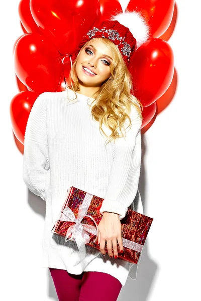 Porträtt av vackra glad söt leende blond kvinna tjej håller i hennes händer stora jul gåva rutan och hjärtat ballonger i casual röda hipster vinterkläder, i vit varm tröja — Stockfoto