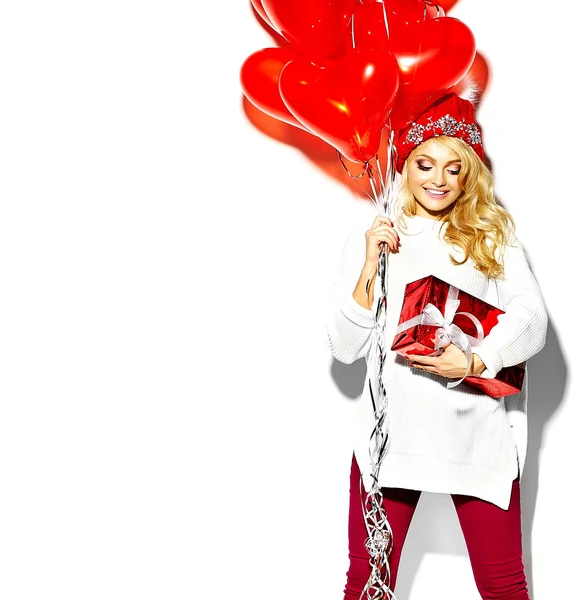 Retrato de hermosa mujer rubia sonriente dulce feliz sosteniendo en sus manos gran caja de regalo de Navidad y globos de corazón en ropa de invierno hipster rojo casual, en suéter blanco cálido —  Fotos de Stock