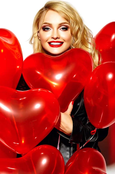 Porträt der schönen, süß lächelnden blonden Frau, die in ihren Händen rote Herzballons in lässiger schwarzer Hipster-Kleidung hält — Stockfoto