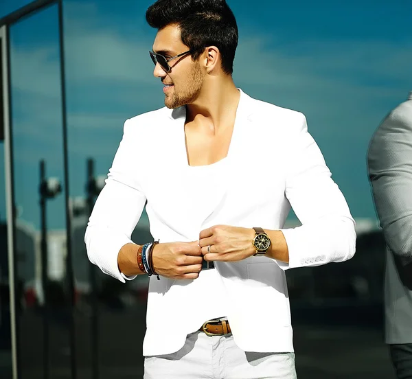 Fashion portrait of young sexy handsome model man in casual white suit in sunglasses in white suit in the street — Zdjęcie stockowe