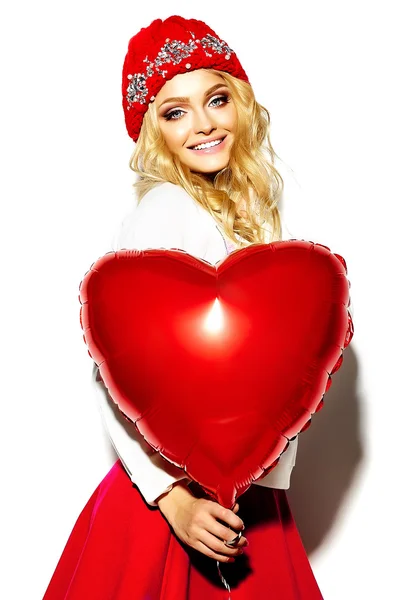 Portrait of beautiful happy sweet cute smiling blonde woman girl in casual hipster clothes, in pink skirt and winter warm beanie with red heart balloon in hands — Stock Photo, Image