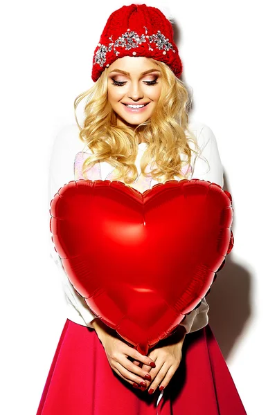 Portrait of beautiful happy sweet cute smiling blonde woman girl in casual hipster clothes, in pink skirt and winter warm beanie with red heart balloon in hands — Stock Photo, Image