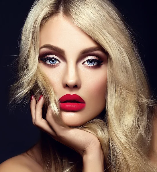 Чуттєвий гламурний портрет красивої блондинки-моделі леді з яскравим макіяжем і червоними губами, що торкаються її обличчя, зі здоровим кучерявим волоссям на чорному тлі — стокове фото