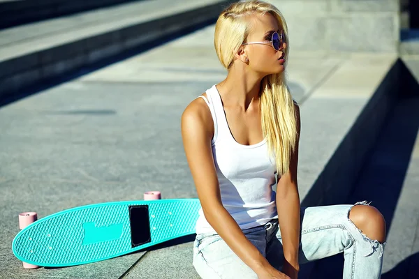 Glamour snygg sexig vacker ung söt blond modell flicka i ljusa casual hipster sommarkläder med skateboard — Stockfoto