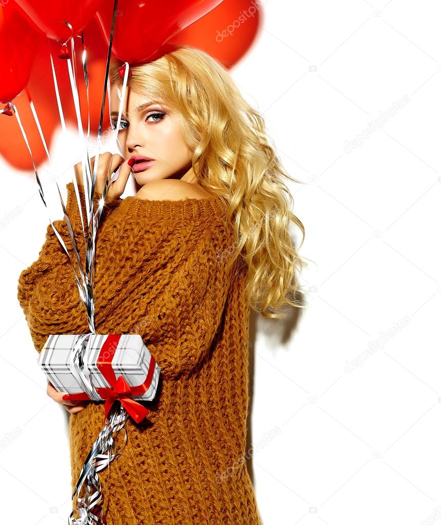 portrait of beautiful happy sweet smiling blonde woman girl holding in her hands Christmas gift box and heart balloons in casual brown hipster winter sweater clothes