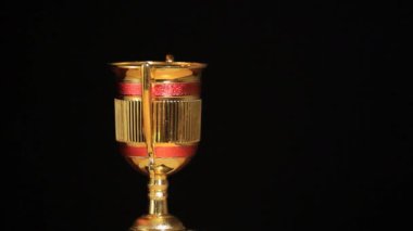 Koyu arkaplanda dönen altın kupa görüntüleri.