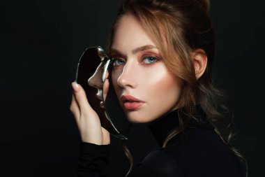 Siyah arka planda kırık aynası olan güzel genç bir kadın.