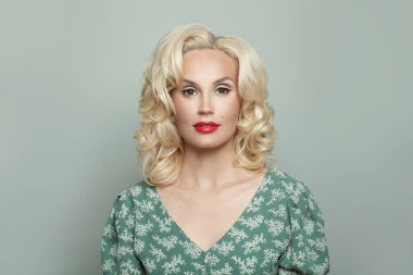 Makyajlı, sarı kıvırcık saçlı, açık yeşil arka planda zarif bir kadın.