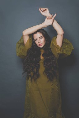 Uzun kıvırcık saçlı, zarif esmer kadın siyah arka planda yeşil tül elbise giyiyor.