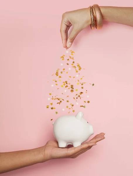 Black woman hands putting in money box golden confetti stars on pastel pink background