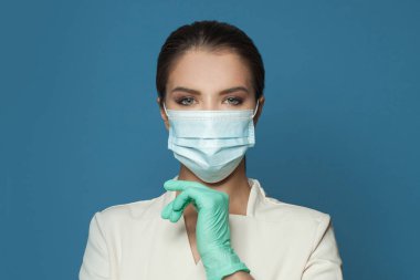 Doktor portresi koruyucu tıbbi yüz maskesi takıyor ve mavi arka planda profesyonel üniforma giyiyor. Tıp, kozmetoloji ve aşı kavramı