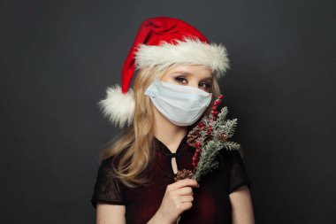 Koruyucu tıbbi maskeli ve Noel Baba şapkalı çekici sarışın kadın. Noel tatili, yeni yıl partisi ve Covid-19 konsepti.