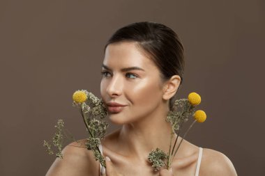 Güzel, sağlıklı bir kadın elinde çiçeklerle kahverengi arka plana bakıyor.