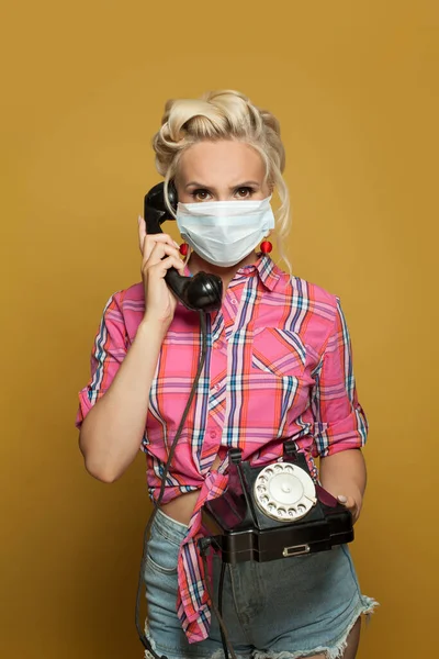 カラフルな黄色の背景にレトロな電話で保護マスクのピンアップ女性 — ストック写真