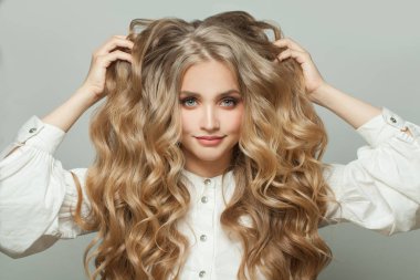 Güzel, gülümseyen bir kadın beyaz arka planda uzun, sağlıklı kıvırcık saçlarına dokunuyor.