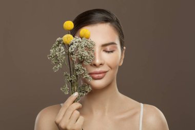 Mükemmel bir cilde ve kahverengi arka planda çiçeklere sahip spa modeli bir kadın. Gözler kapalı. Bitkisel ilaçlar ve cilt bakımı