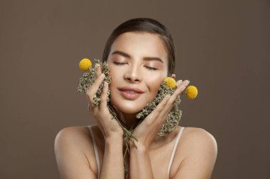 Kahverengi arka planda parlak, berrak bir teni olan çekici bir kadın. Yüz bakımı, bitkisel ilaçlar ve cilt bakımı konsepti