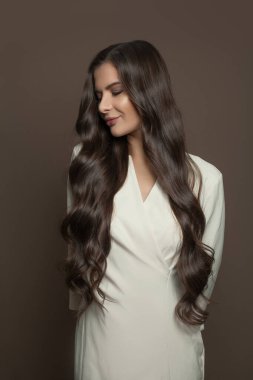 Uzun siyah saçlı, beyaz elbiseli, kahverengi arka planda duran hoş bir kadın.