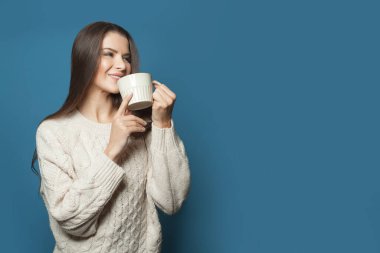 Mutlu genç bir kadın mavi afişte kahve içiyor.