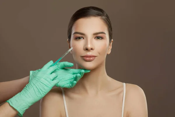 Beautiful woman face with syringe injection on brown background. Cosmetology and aesthetic surgery concept