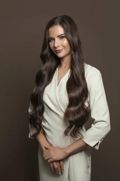 Friendly woman with long dark hairstyle standing on brown background