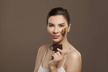 Kahverengi arka planda çikolata fırçası olan gülümseyen kadın. Yüz bakımı, spa sağlığı ve cilt bakımı konsepti