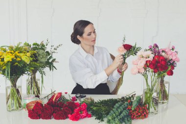 Beyaz arka planda çiçeklerle çalışan çiçekçi kadın.