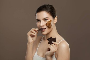 Kahverengi arka planda çikolatadan hoşlanan güzel bir kadın. Yüz bakımı, spa sağlığı ve cilt bakımı konsepti