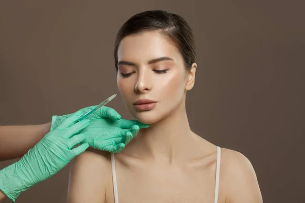 Beautiful woman face with syringe injection on brown background. Cosmetology and aesthetic surgery concept