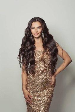 Makyajlı, uzun kıvırcık saçlı, beyaz arka planda altın gece elbisesi giyen mükemmel esmer kadın.