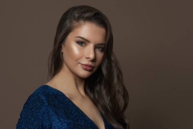 Sağlıklı genç bir kadın yüzü, parlak berrak bir ten, uzun kıvırcık saçlar ve kahverengi arka planda doğal makyaj.