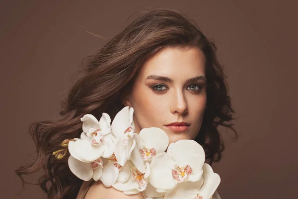 健康な茶色の髪 澄んだ肌 自然なメイクと白い蘭の花の肖像画と若いかわいい女性の顔 — ストック写真