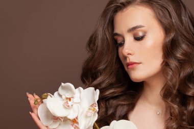 Sağlıklı, açık tenli, kahverengi kıvırcık saçlı ve beyaz orkide çiçekleri olan güzel bir kadın model. Yüz bakımı ve cilt bakımı kavramı