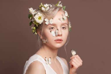 Beyaz bahar çiçekleri ve kahverengi arka planda kelebekleri olan mükemmel bir genç kadın.