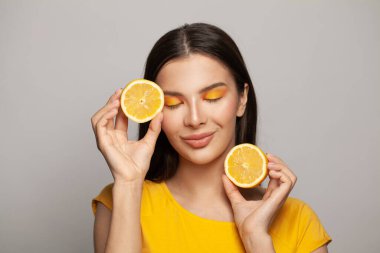 Gülümseyen esmer kadın beyaz arka planda sarı limon meyveleri tutuyor.