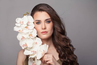 Uzun ve gür dalgalı saçlı esmer kadın. Beyaz orkide çiçekleri tutan kıvırcık saçlı güzel bir manken. .