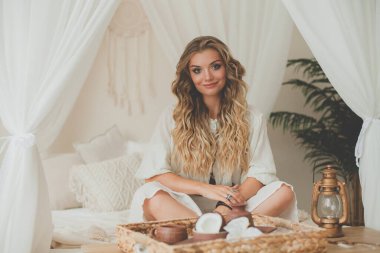 Sarışın, kıvırcık saçlı çekici bir kadının portresi. Tropik bir tatil köyündeki otel odasında dinleniyor.