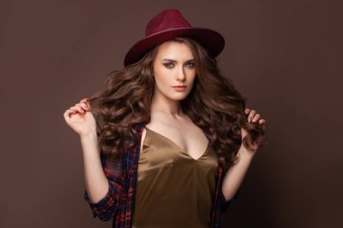 Uzun kıvırcık saçlı güzel bir kadın yüzü. Kahverengi arka planda fötr şapkalı kadın model
