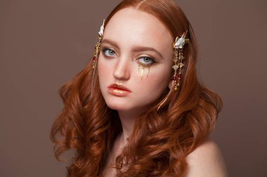 Kahverengi arka planda yaratıcı makyajlı kızıl saçlı kadın.