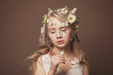 Çıplak makyajlı çekici bir kadın, mükemmel sağlıklı bir cilt ve elinde kelebek tutan beyaz bir çiçek.