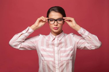 Genç, güzel, neşeli bir kadının portresi. Gözlüklerle gülümseyen. Kırmızı arka plandaki kameraya bakıyor.