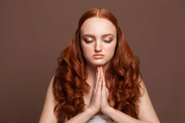 Young woman with closed eyes praying on brown background
