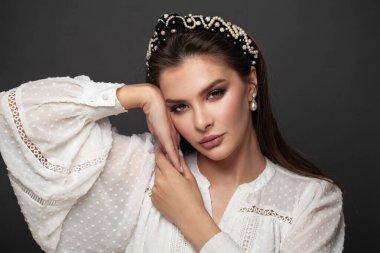 Siyah saç bandı ve siyah arka planda inci küpeli güzel esmer kadın.