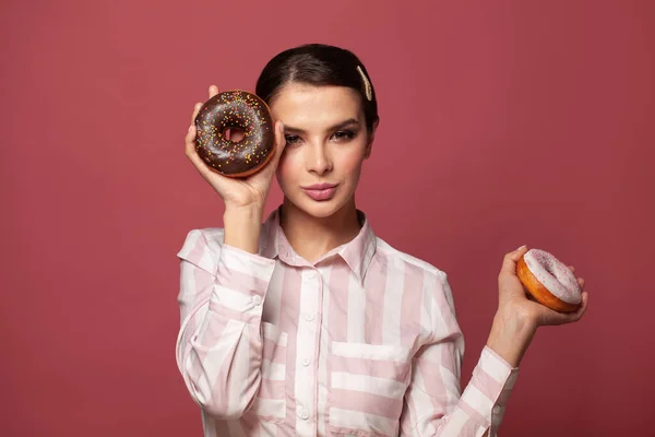 Beauty fashion model woman taking colorful sweets donuts. Diet, dieting, junk food, slimming and weight loss concept. Funny woman with sweets on pink background.