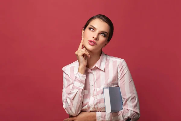 Thinking woman in glasses with book. Student woman looking up and thinking on red banner background