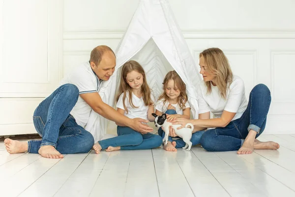 Mutlu genç anne ve baba ve iki küçük kızı yerde oturmuş yavru köpek evcil hayvanlarına bakıyorlar.