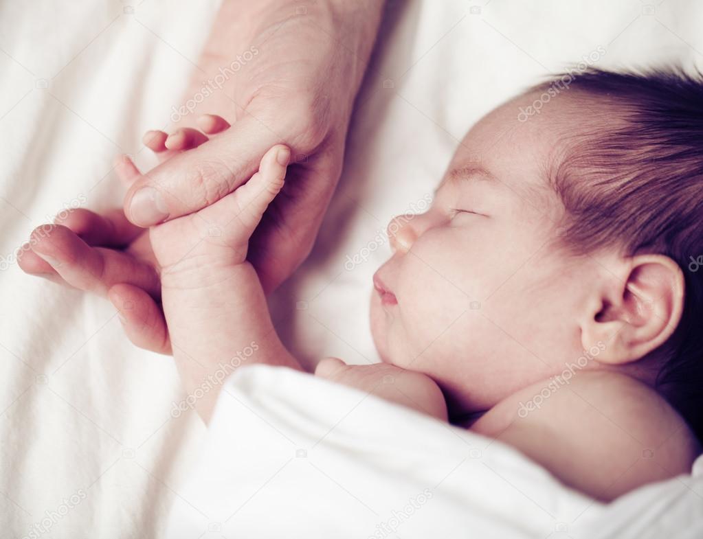 Newborn baby and his father's hand