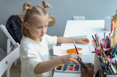 Evde resim yapan neşeli genç bir çocuk. İçerideki küçük kızın yakın plan portresi.