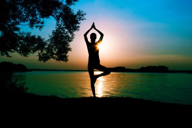 Gün batımında sahilde poz yoga uygulamak siluet kadın