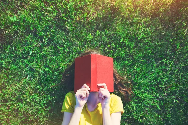 Mädchen liest Buch im Gras liegend. — Stockfoto